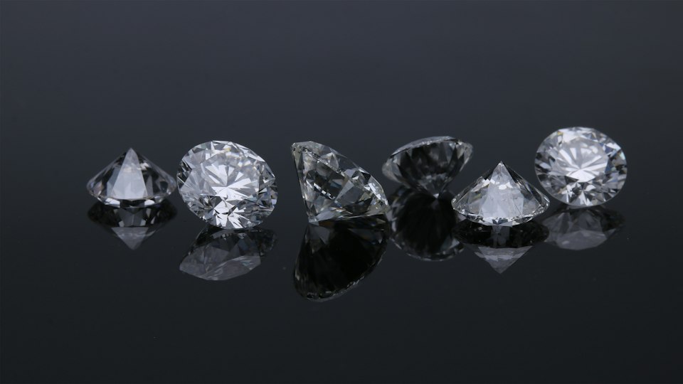 Six round brilliant diamonds in a row on a dark reflective surface